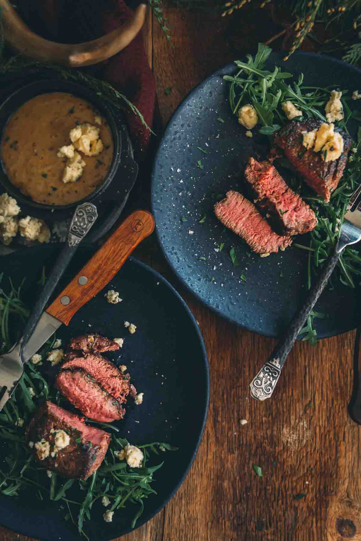 Overhead shot of plates with sliced sous vide filet mignon steaks on beds of greens with blue cheese.