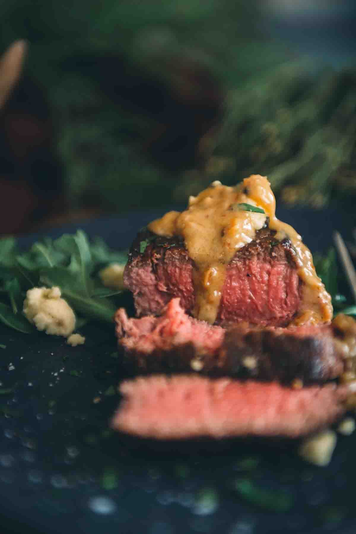 Sliced medium rare rosy pink tenderloin filet with sauce drizzled over top. 