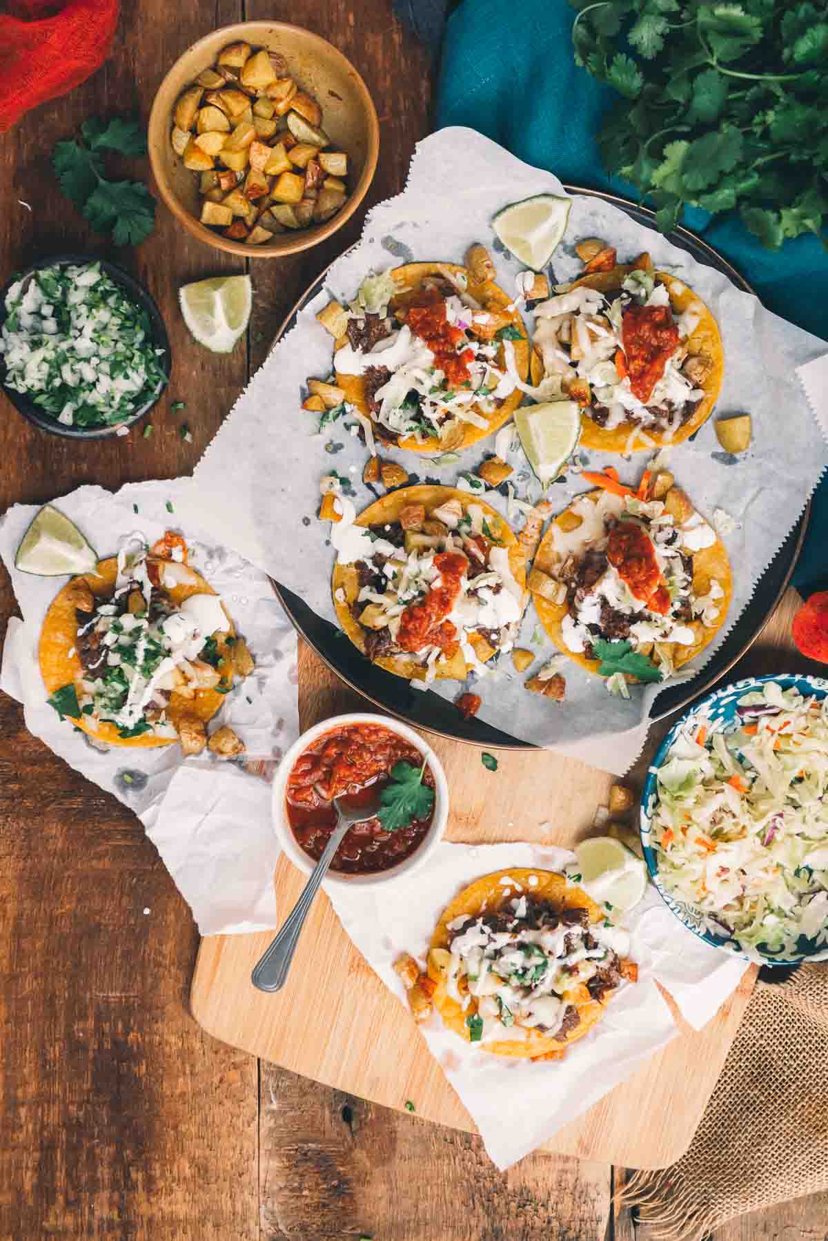 Overhead shot of platter of messy garnachas with toppings scattered about from salsa to lime wedges for a fun and festive photo.