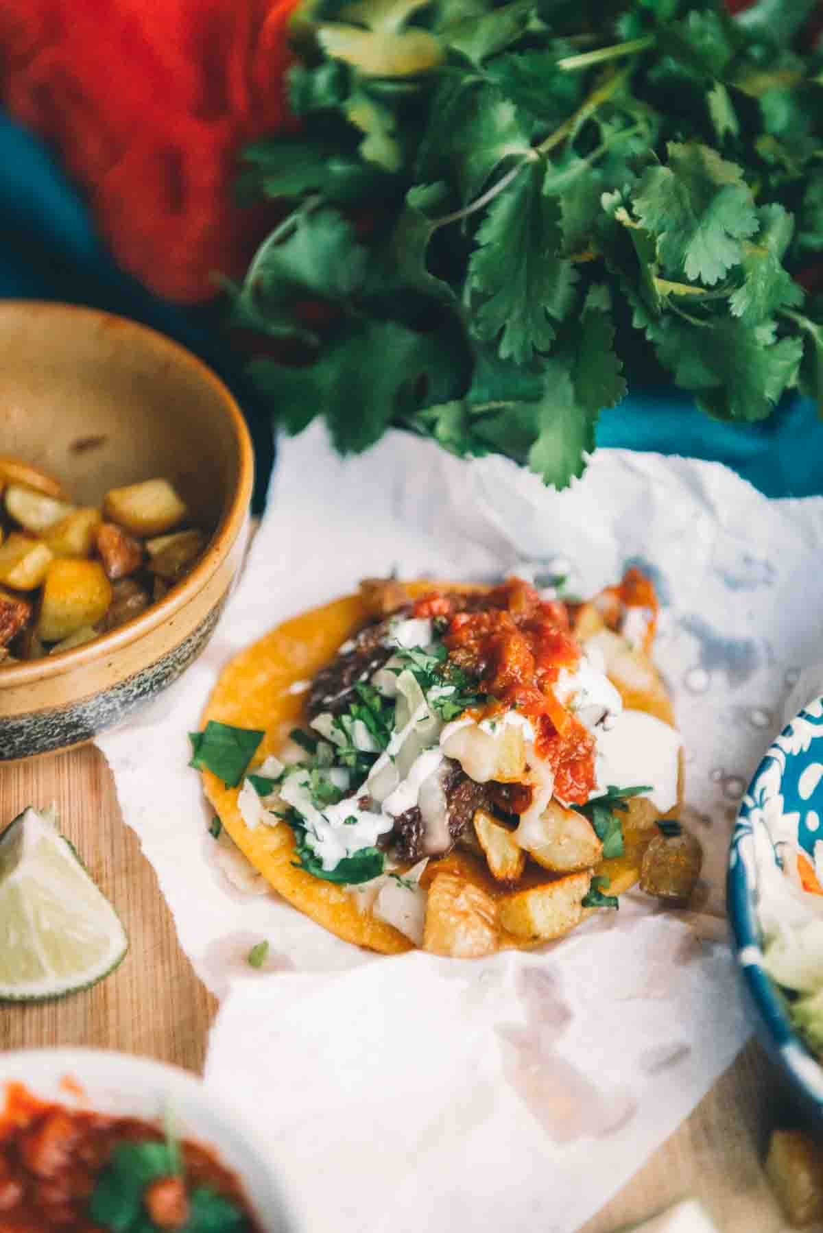 Close up of shredded beef and potatoes on a crispy fried corn tortilla topped with minced onion, salsa, and crema.