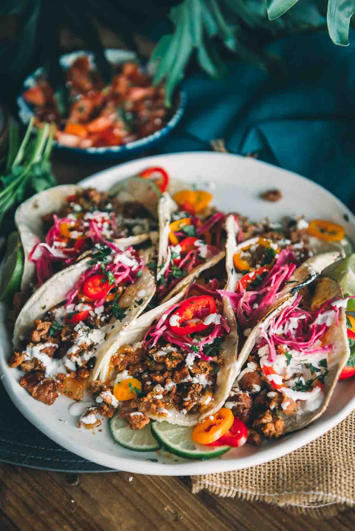 Ground pork tacos arranged on a plate with colorful fresh toppings lime minced peppers and pickled red cabbage. 