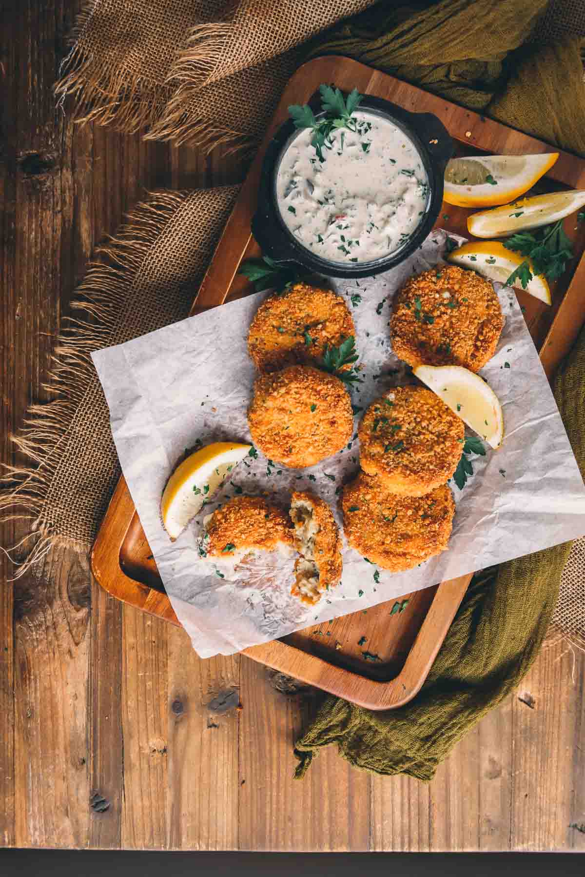 Overhead shot of platter of golden brown crispy fried fish patties garnished with lemon wedges and minced herbs. 
