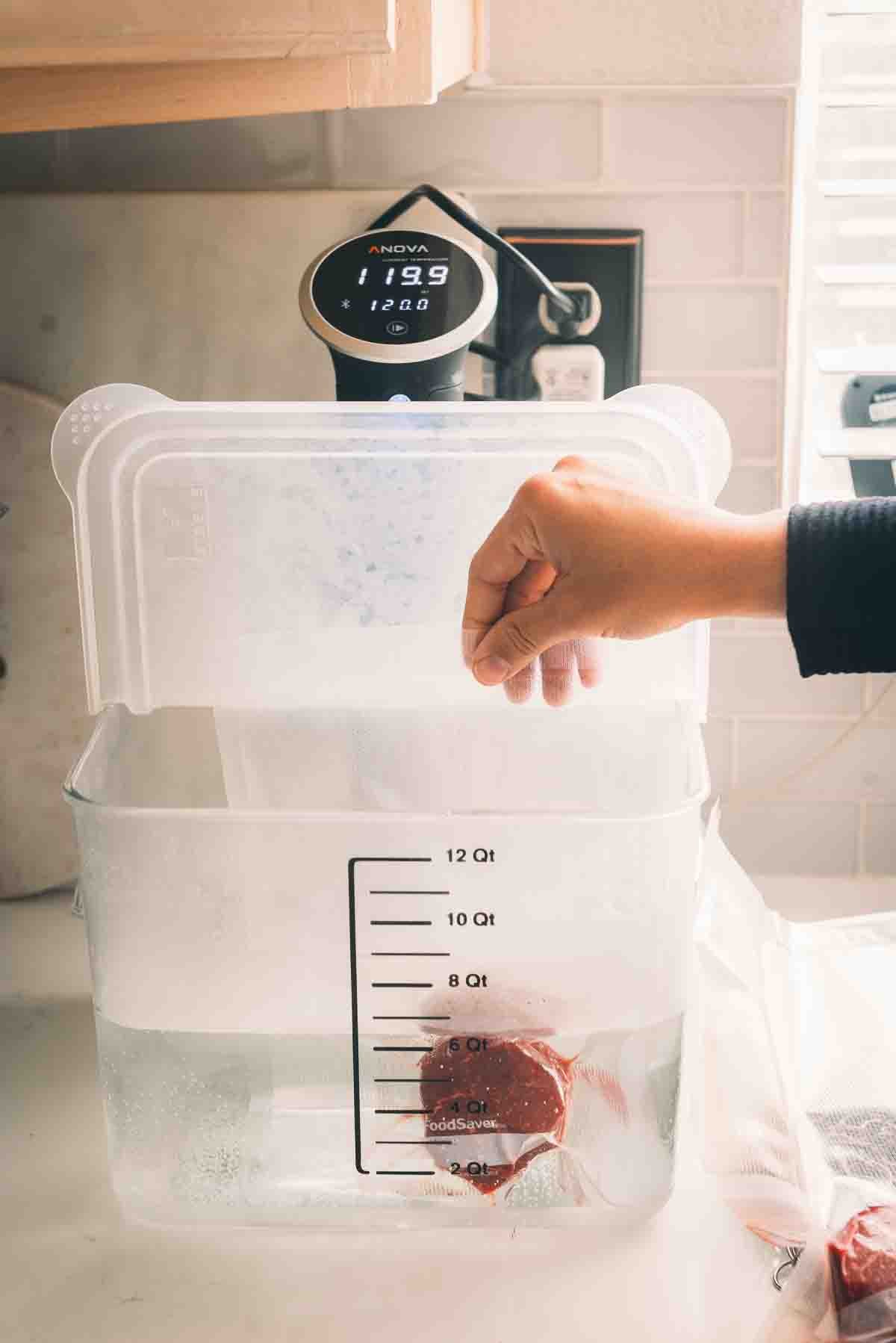 Hand placing steak in sous vide bath.