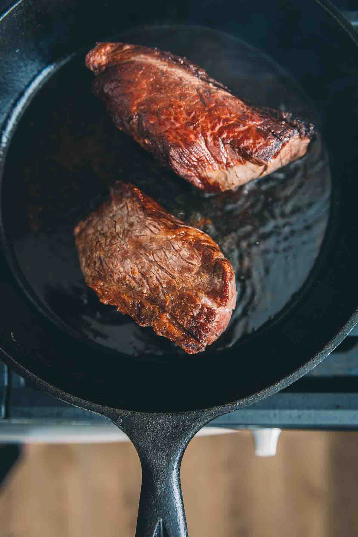 Overhead of steaks in a cast iron pan to show sear. 