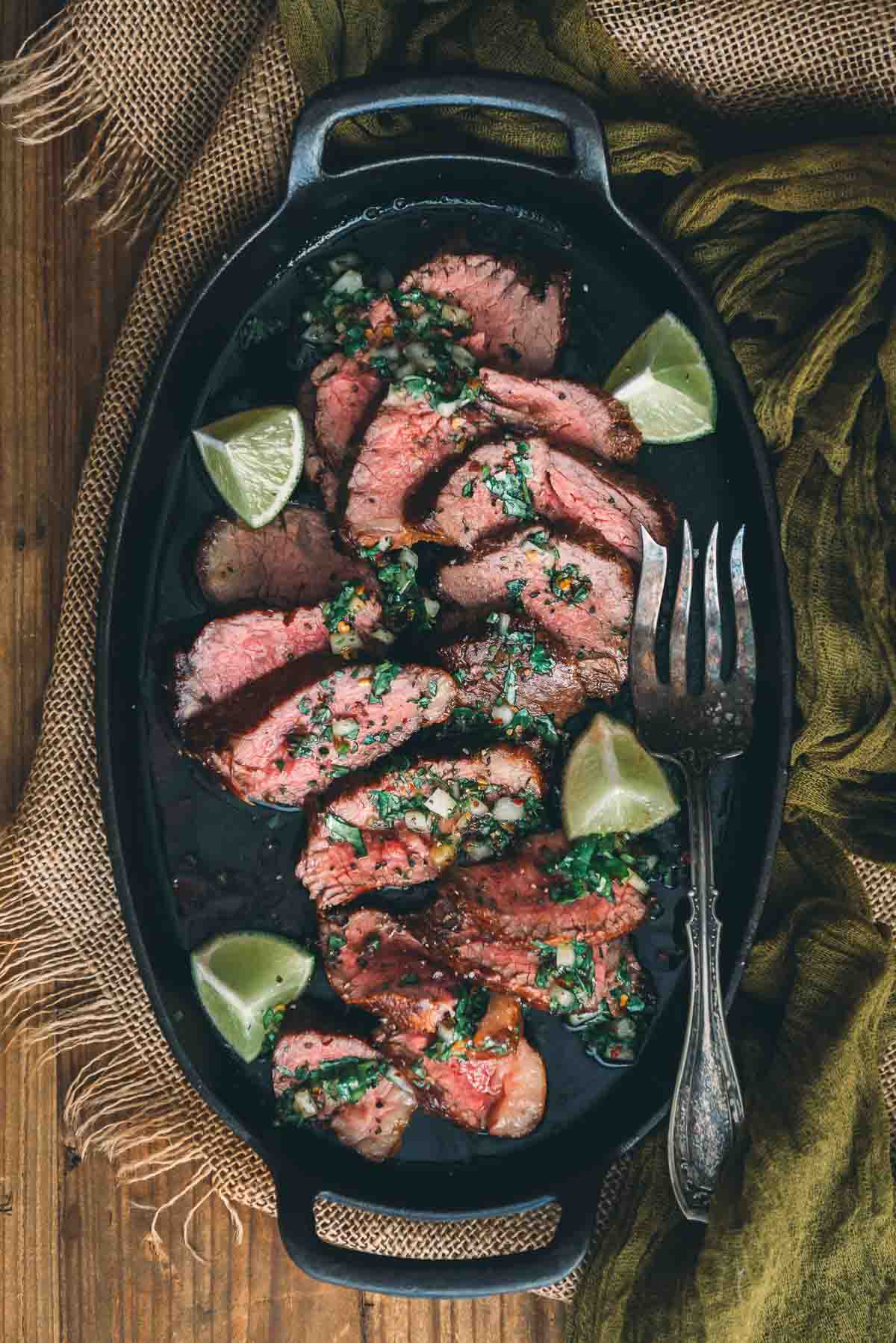 Overhead shot of sliced medium rare steaks on  cast iron pan drizzled with vibrant chimichurri. 