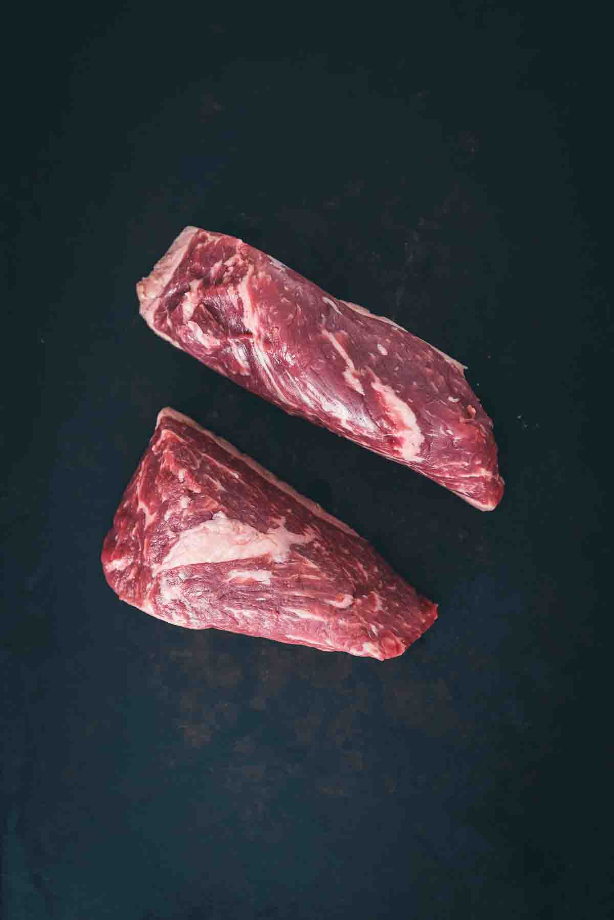 Tri-tip steaks, also called Newport steaks, displayed on a black background to show how uneven they are and the internal marbling. 