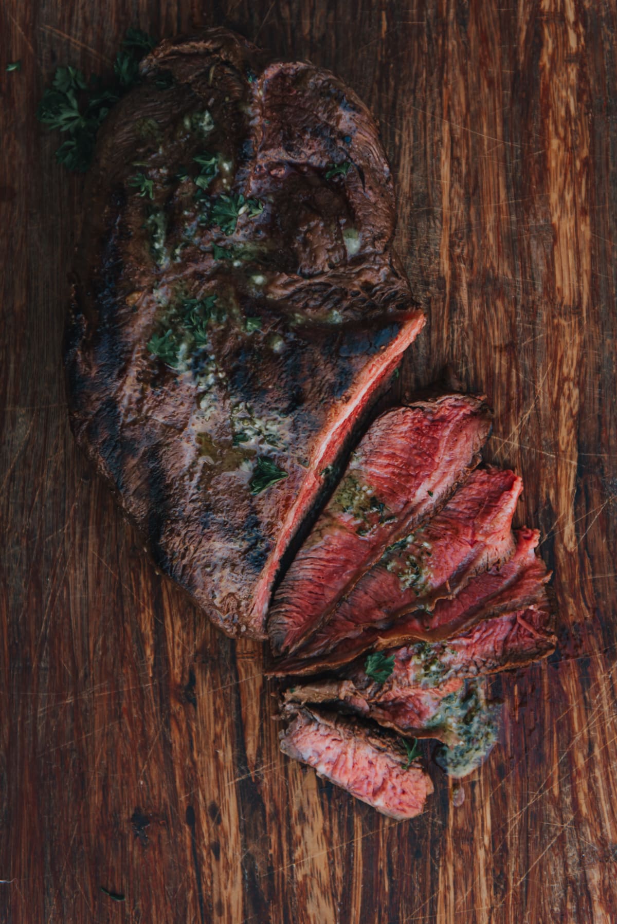 Grilled flat iron steak sliced to show medium rare center, topped with homemade chimichurri. 