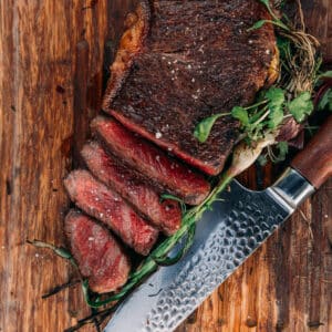 Ribeye steak sliced on a cutting board with a knife.