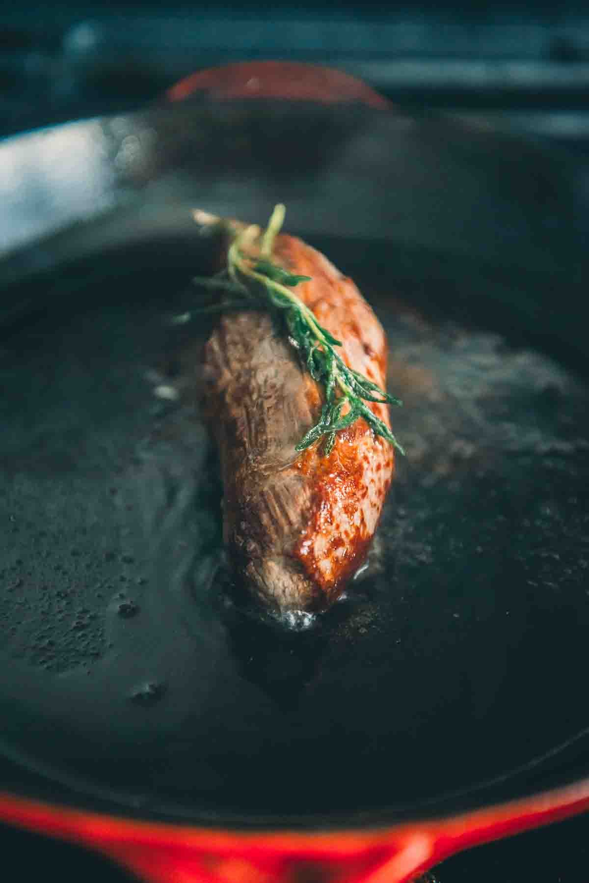 Petite tender steak searing in cast iron pan. 