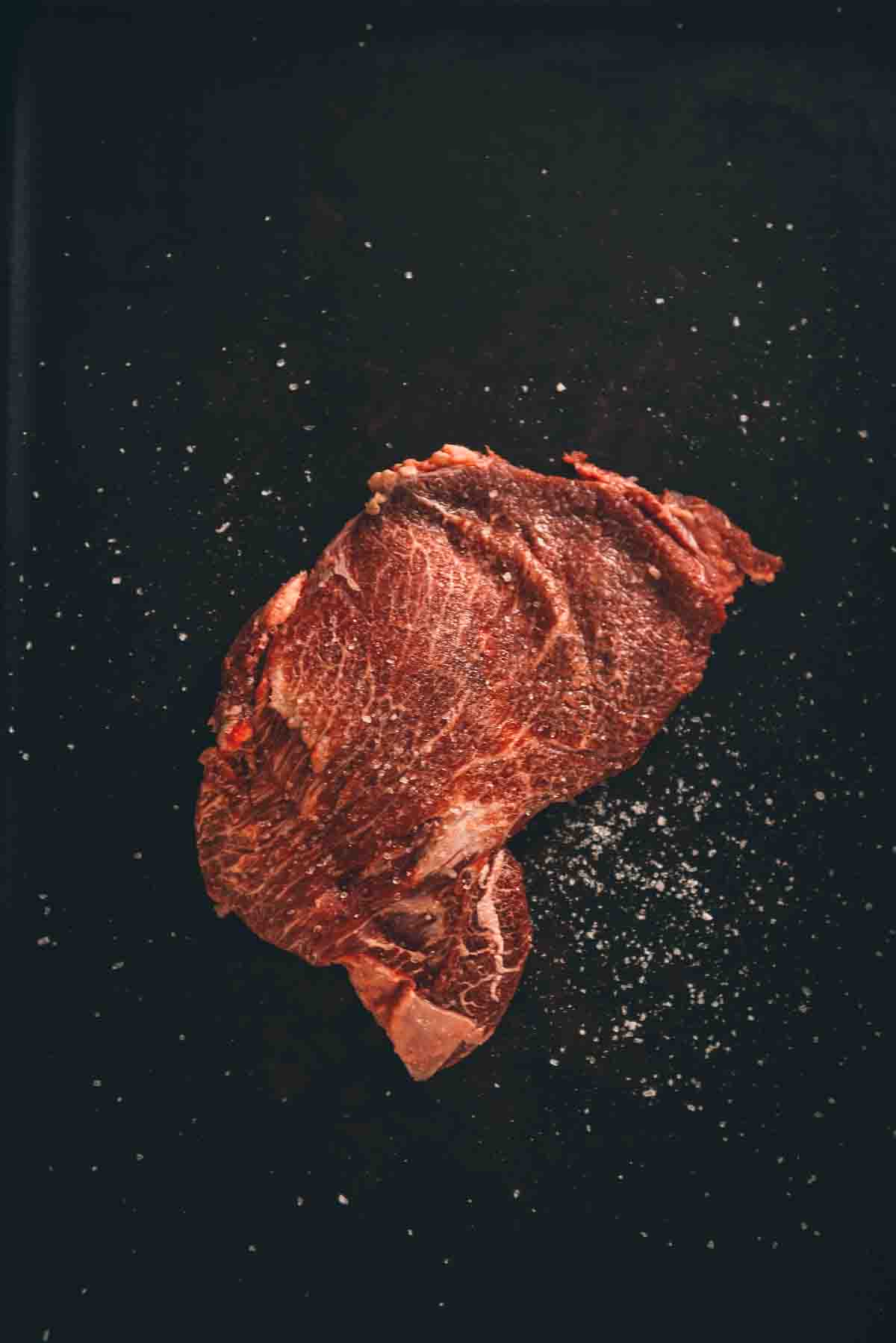Beef cheek on a black background seasoned with salt. 