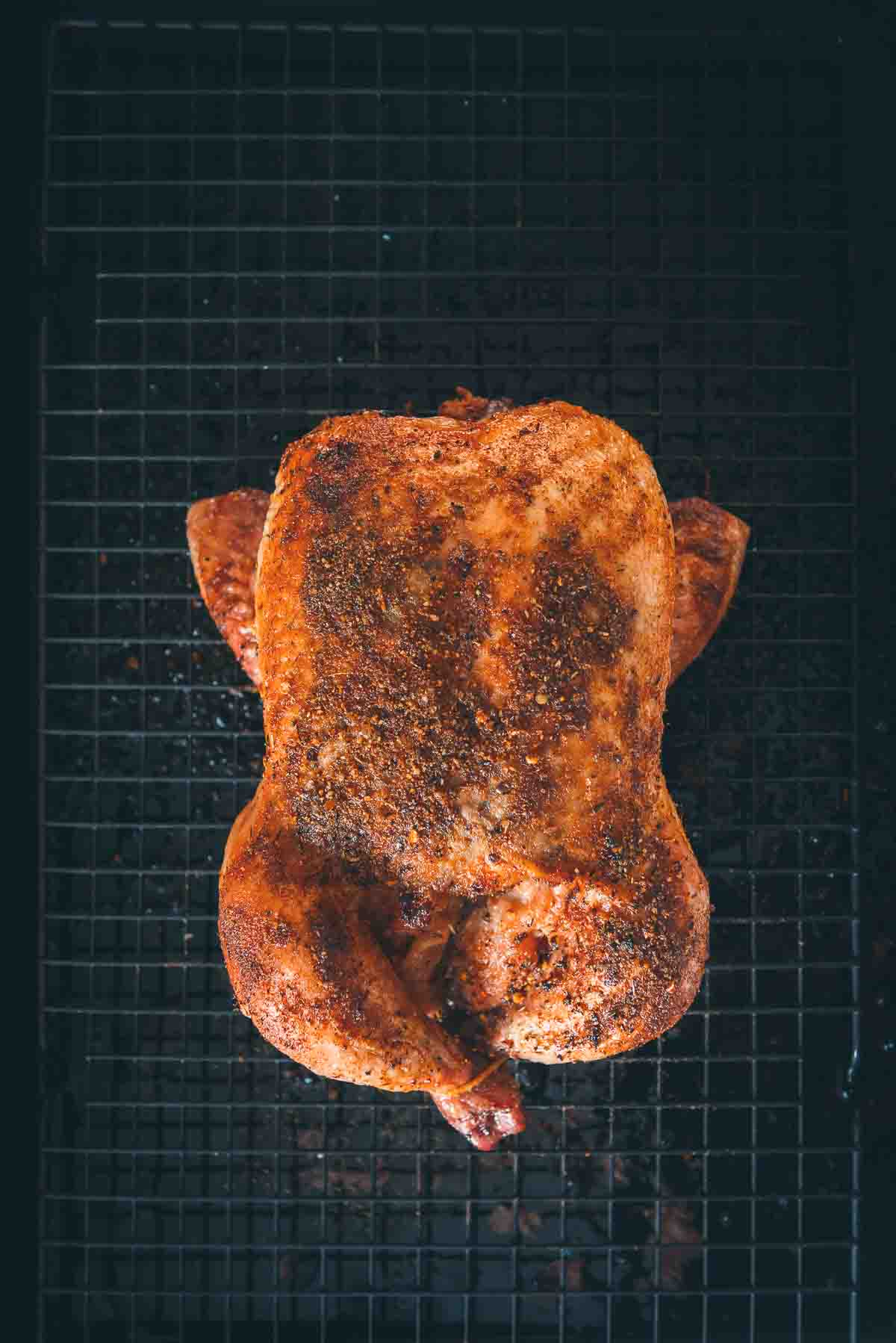 Whole smoked chicken resting on a wire rack. 