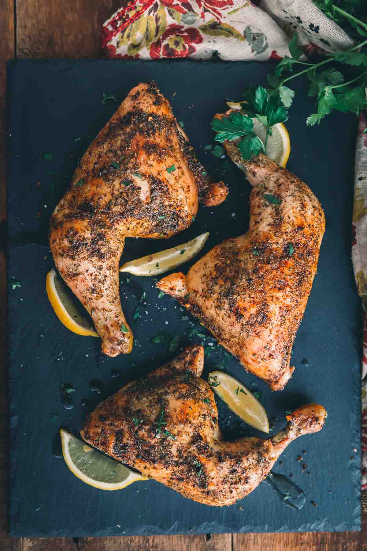 Overhead image of golden brown chicken quarters with crispy skin on a black serving plate.