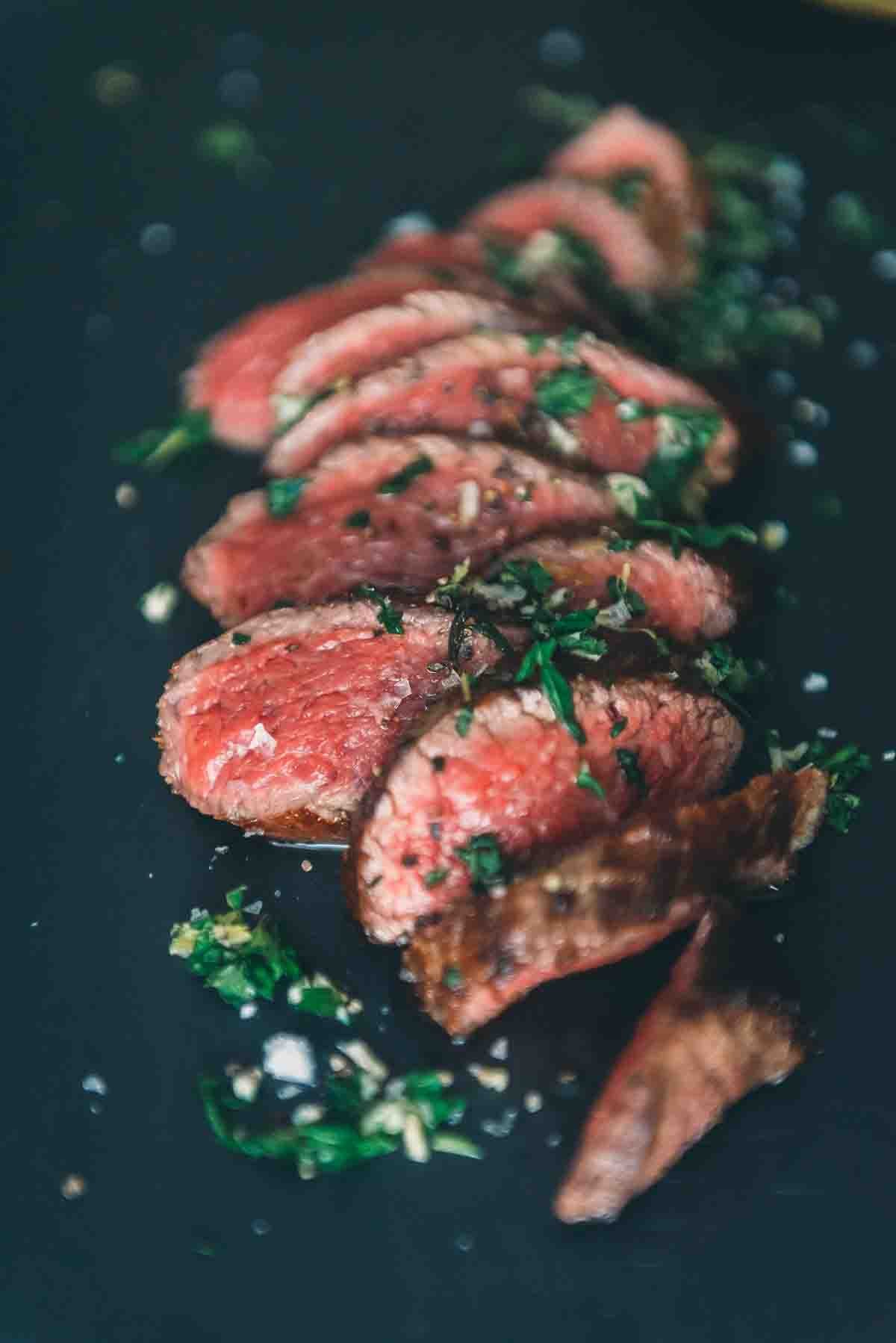 Close up of rare slices of meat with gremolata sprinkled on top. 