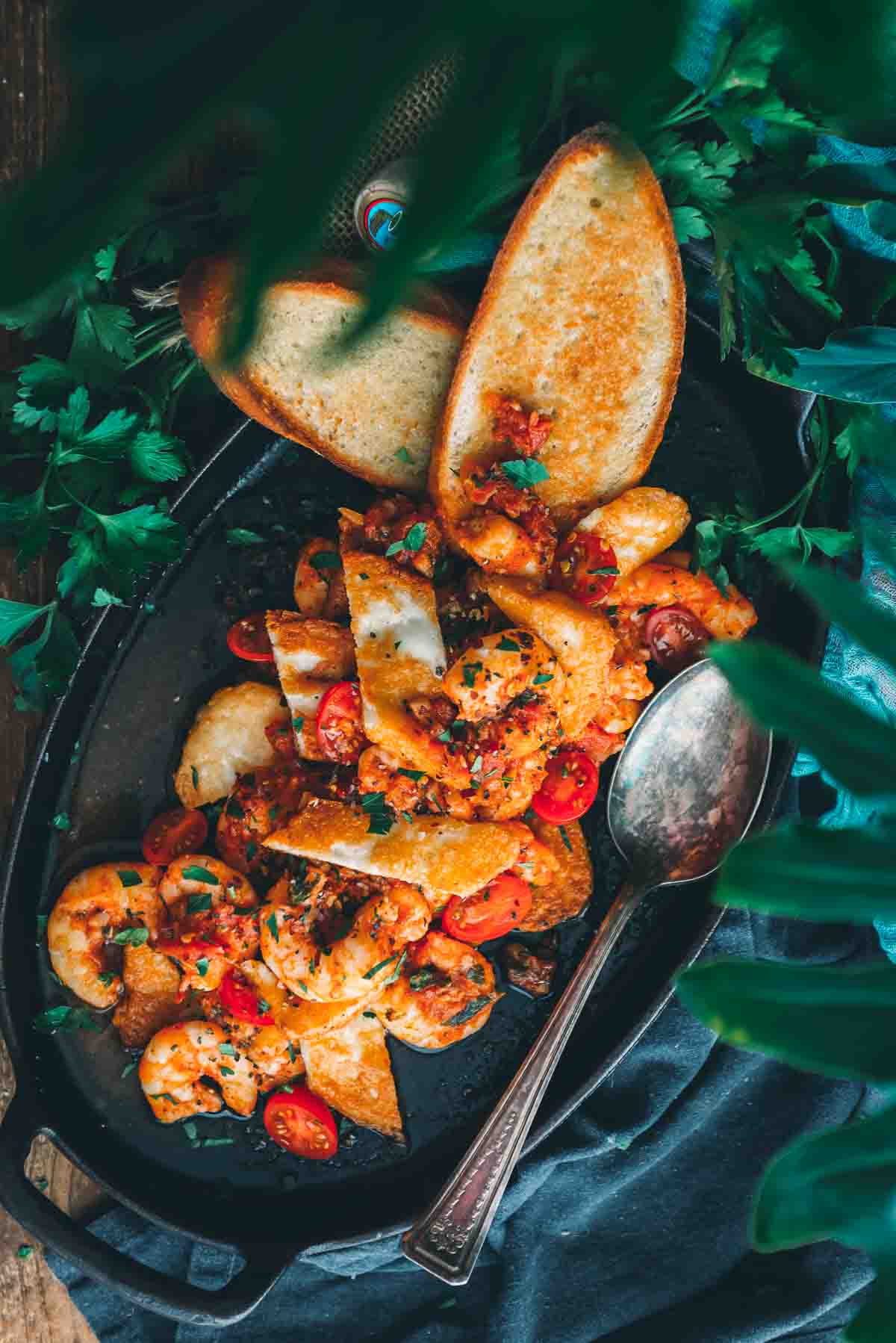 Overhead shot of colourful fresh cook shrimp saganaki with fried cheese on a cast iron serving platter. 