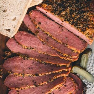 Sliced smoked corned beef and pickles on a cutting board.