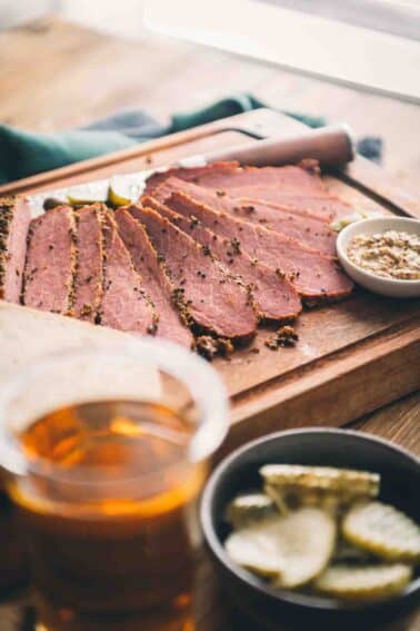 Ham and pickles on a wooden cutting board with smoked corned beef.