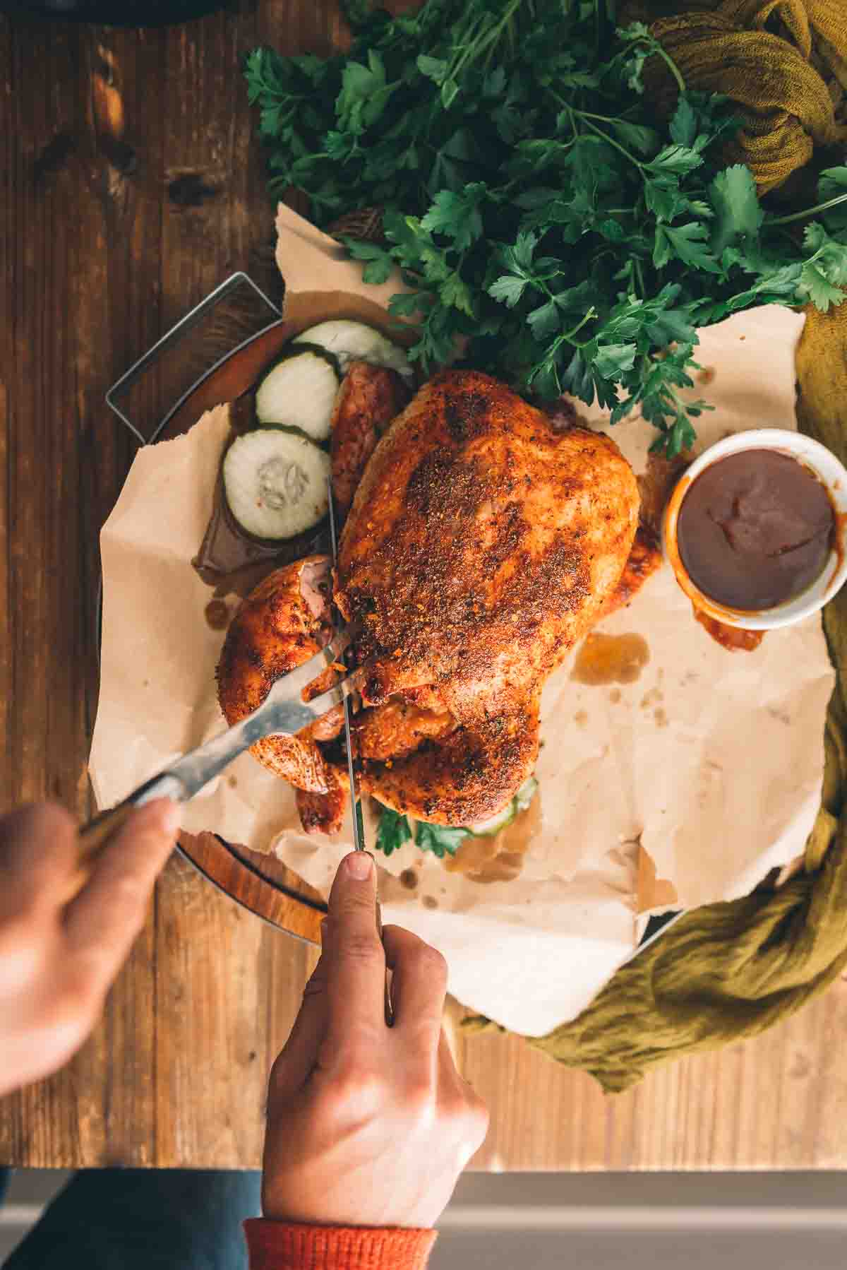 Hands holding a knife and fork slicing the drum from the whole chicken. 