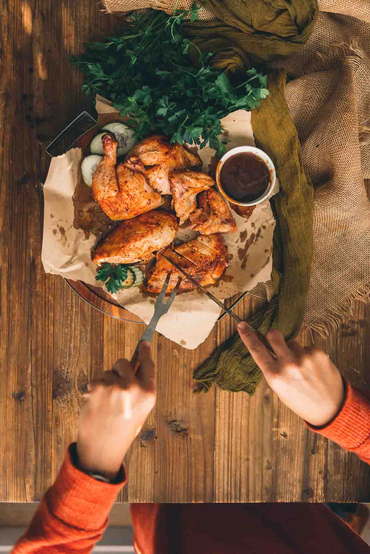 Hands holding knife and fork slicing a chicken breast into strips. 