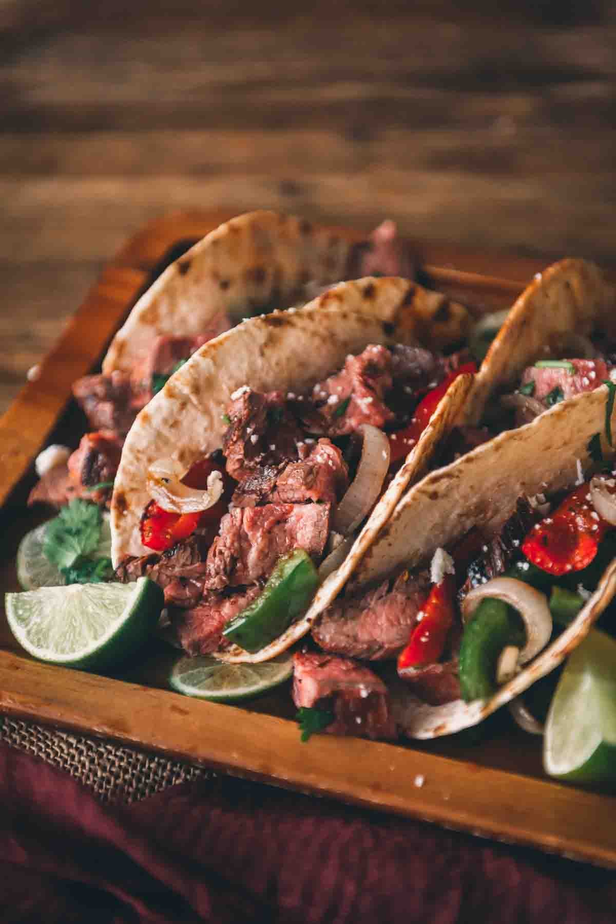 Close up of chopped steak in a folded tortilla with grilled veggies and limes. 