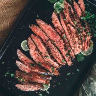 Grilled flank steak on a black baking sheet.