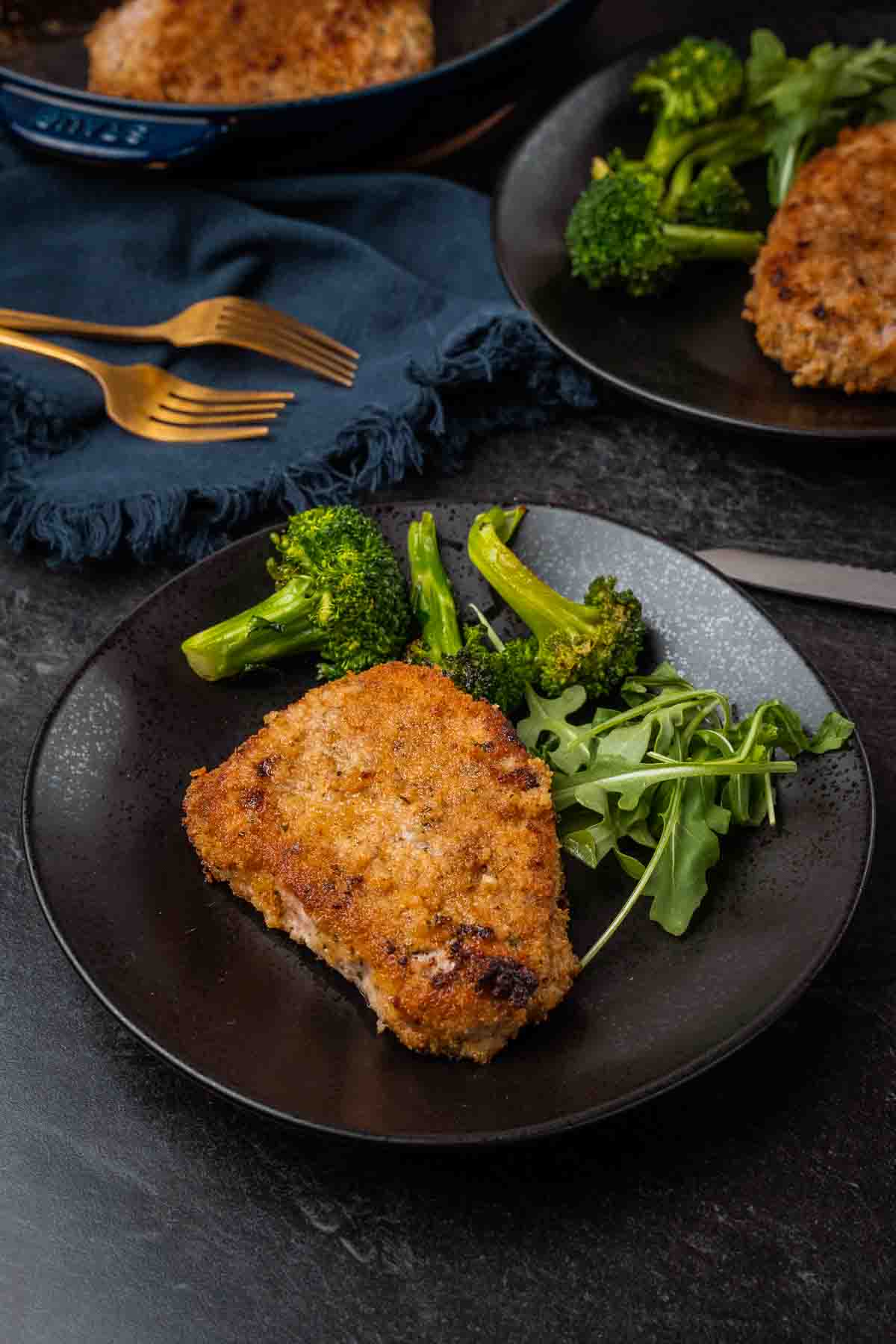 Crispy baked pork chop on a black plate with green veggies. 