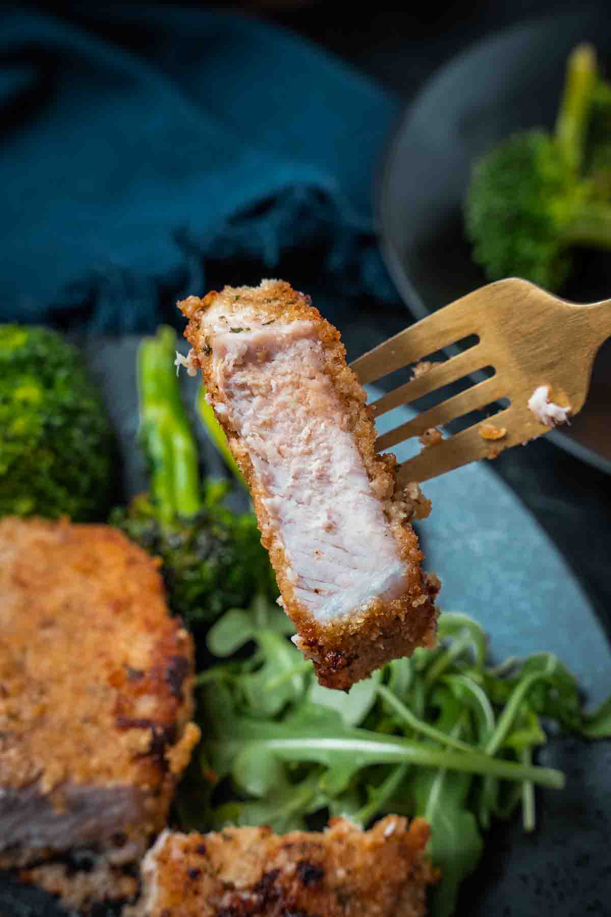 Fork holding a piece of pork to shop crispy exterior and tender perfectly cooked meat. 