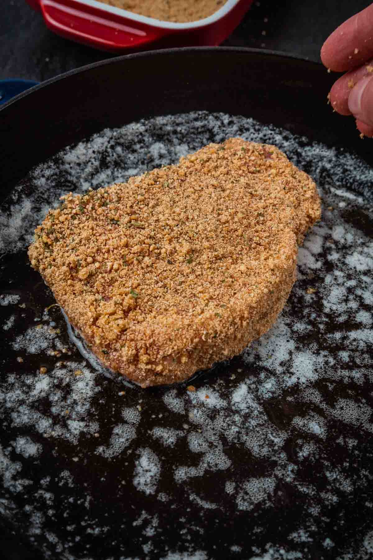 Breaded chop placed in skillet with melted butter. 