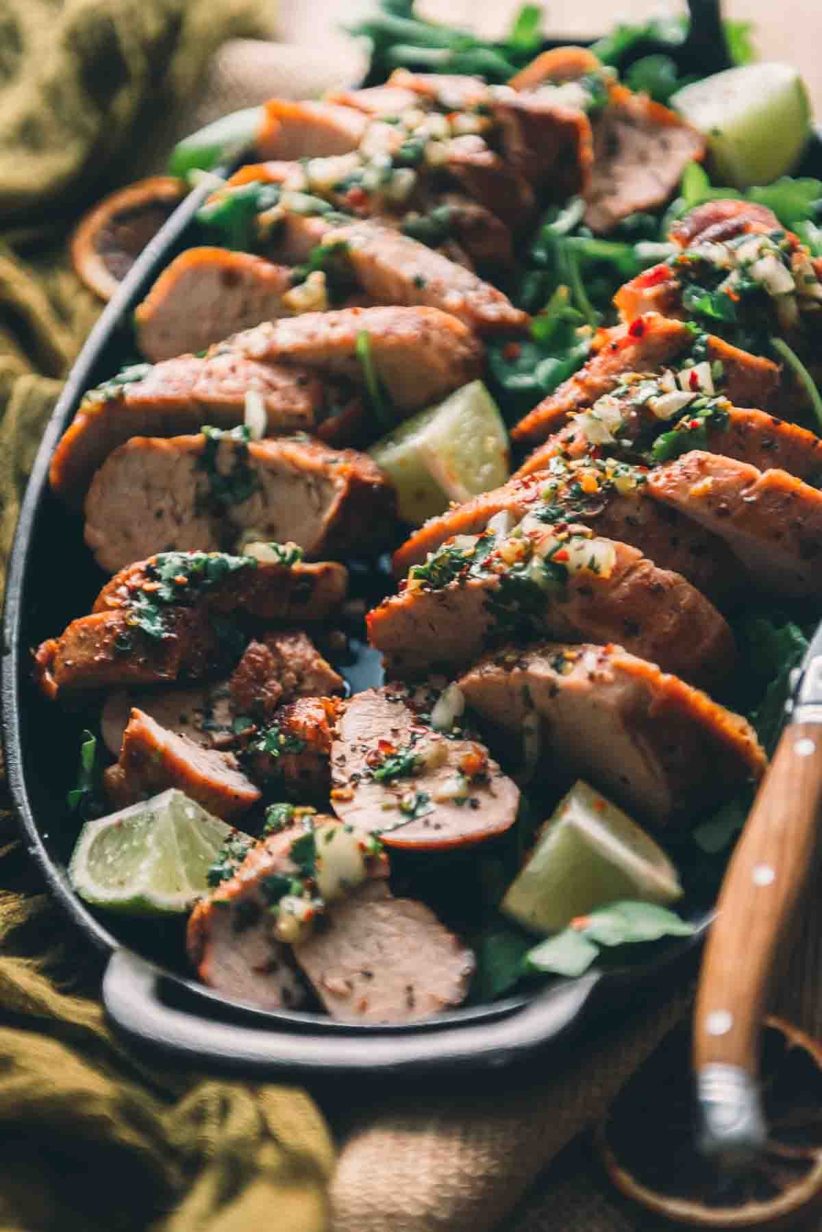 Backlight sliced roasted pork garnished with chimichurri and limes. 