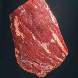 A flank steak on a black surface.