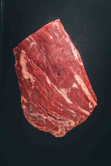 A flank steak on a black surface.