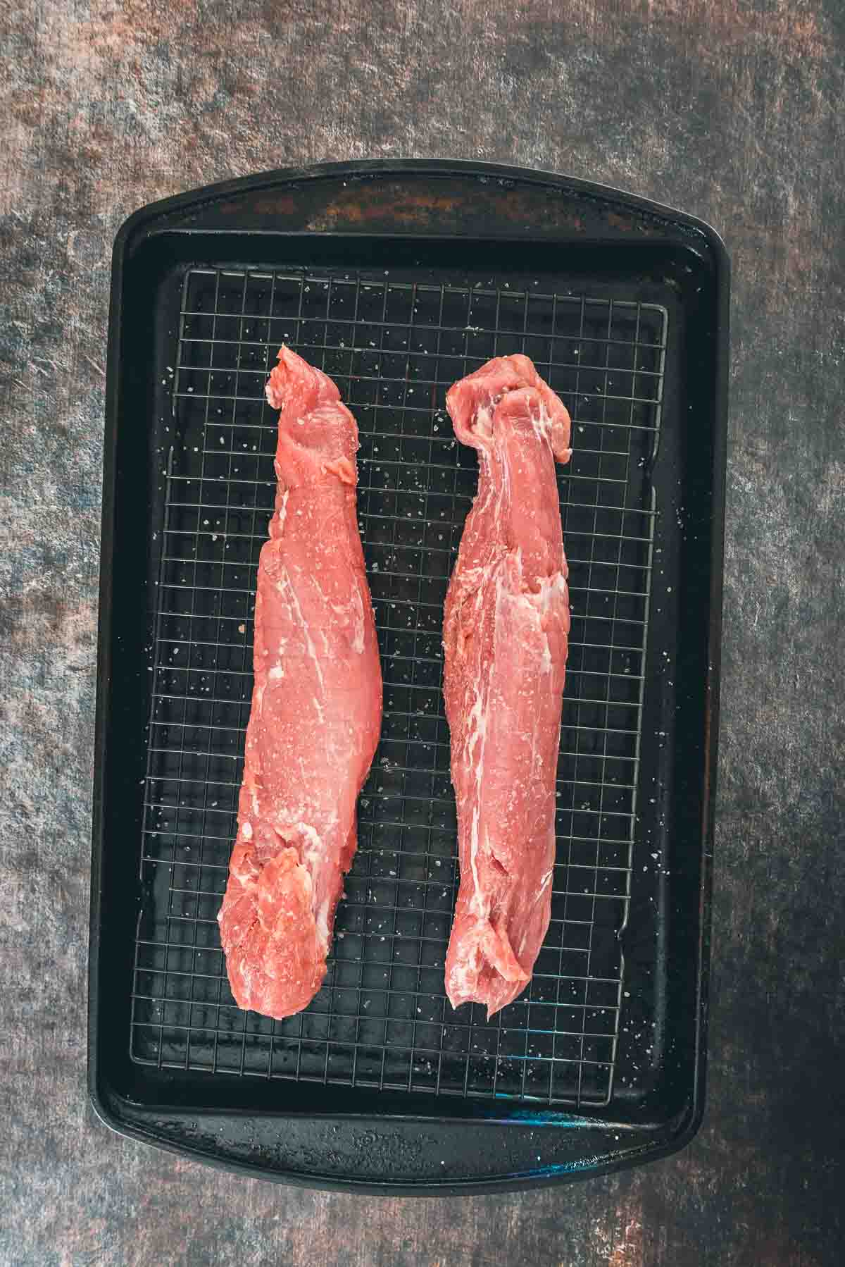 Overhead shot of pork tenderloins on a black baking sheet.