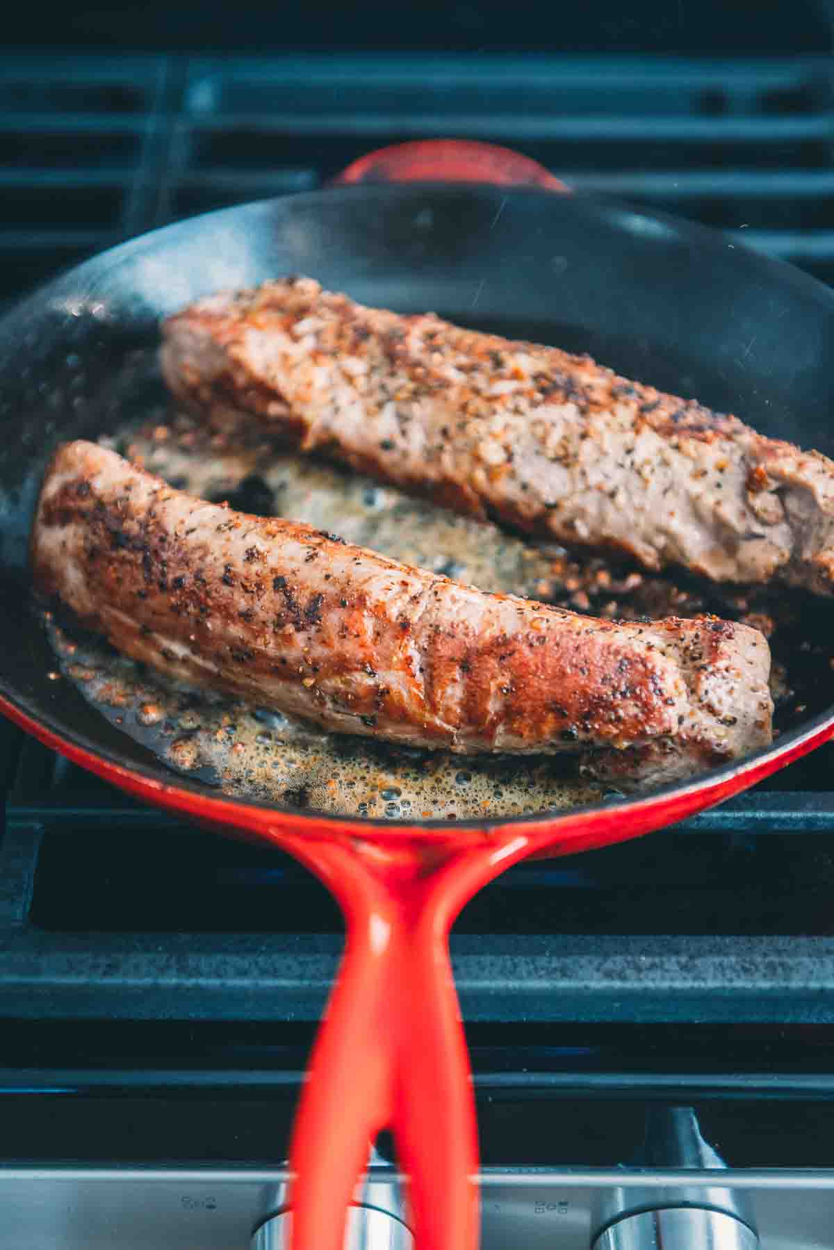 Tenderloins being seared in a hot pan, showing browning. 