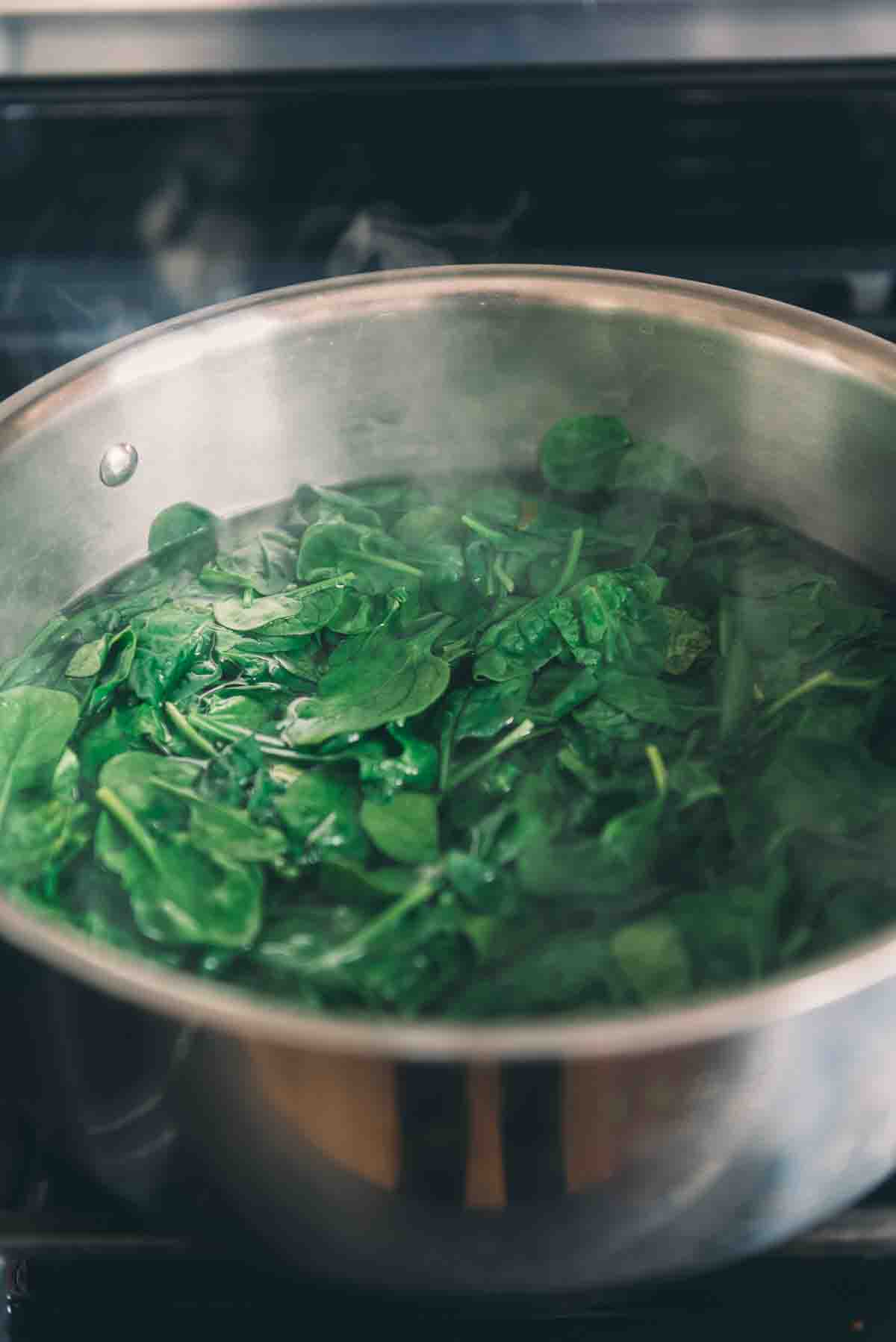 Spinach being blanched in a pot of hot water.