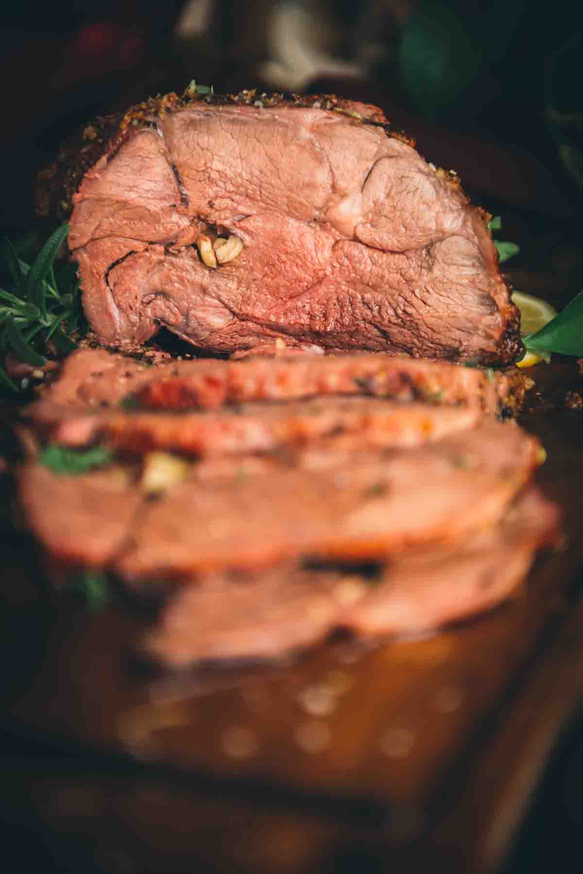 Close up of lamb roast, sliced to show the center with garlic cloves inside. 