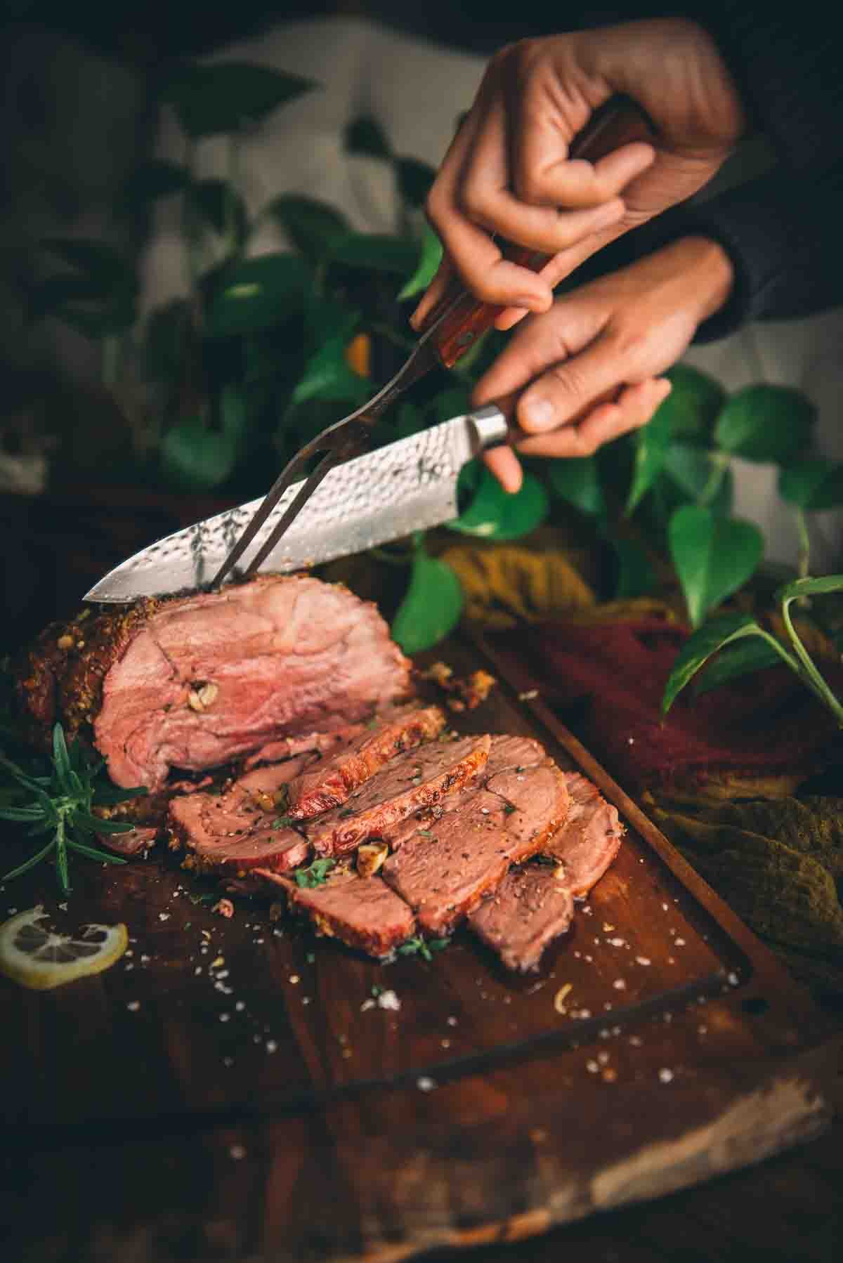 Hands holding fork and knife carving smoked lamb. 