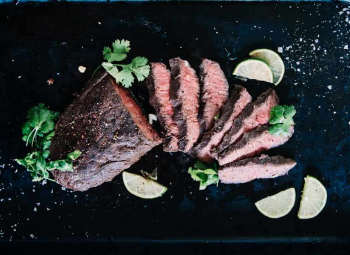 A piece of steak on a black plate with lime wedges.