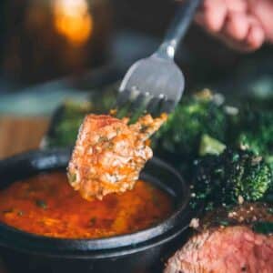 Close up of fork holding piece of steak just dipped in the sauce.