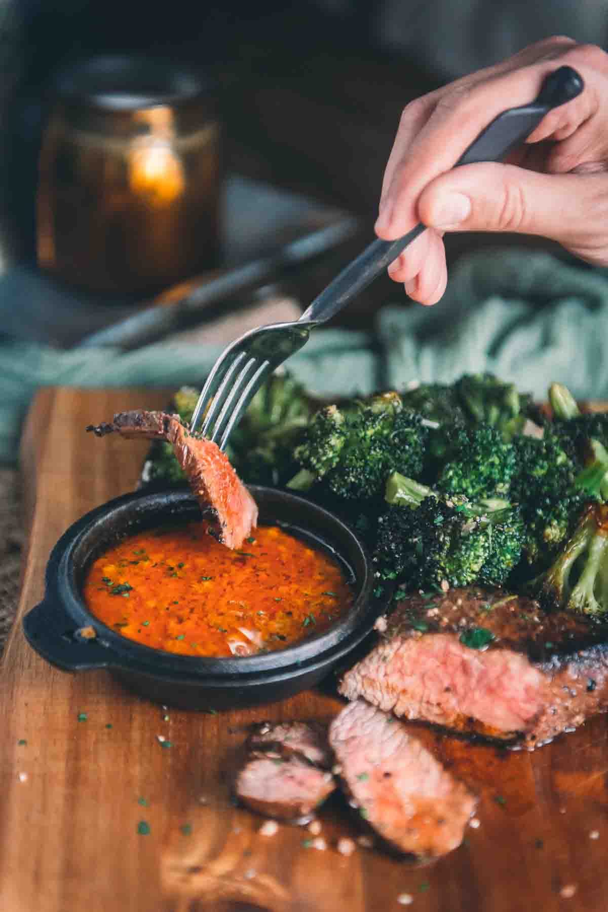 Hand with a fork and slice of meat about to dip into the sauce. 