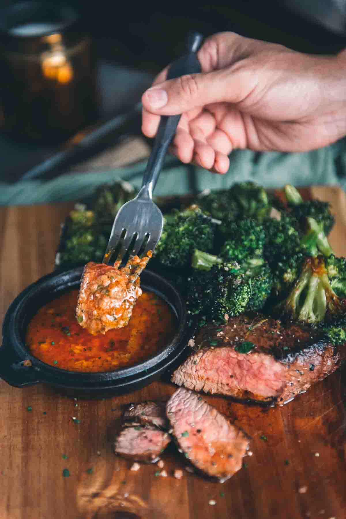 Hand holding fork with piece of meat on it just dipped into the butter sauce. 