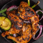Grilled chicken in marinade on a black plate.