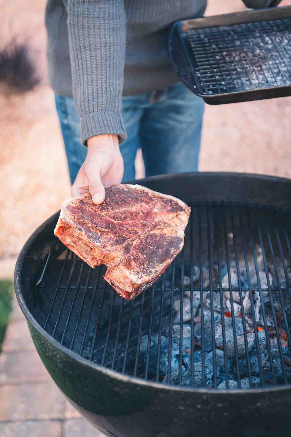 Hand putting steak on the grill. 