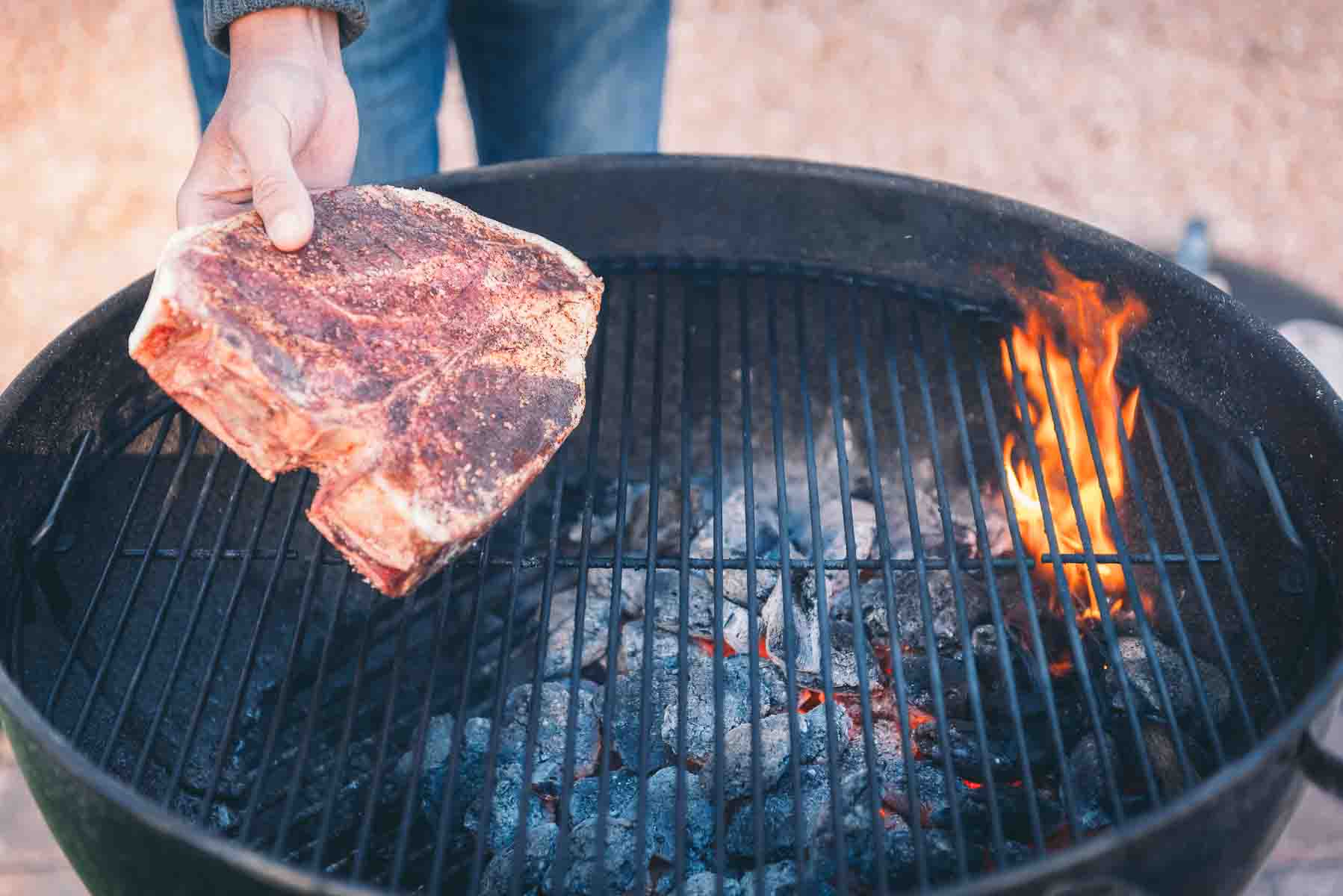 Porterhouse steak being placed on the cooler side of the charcoal grill. 