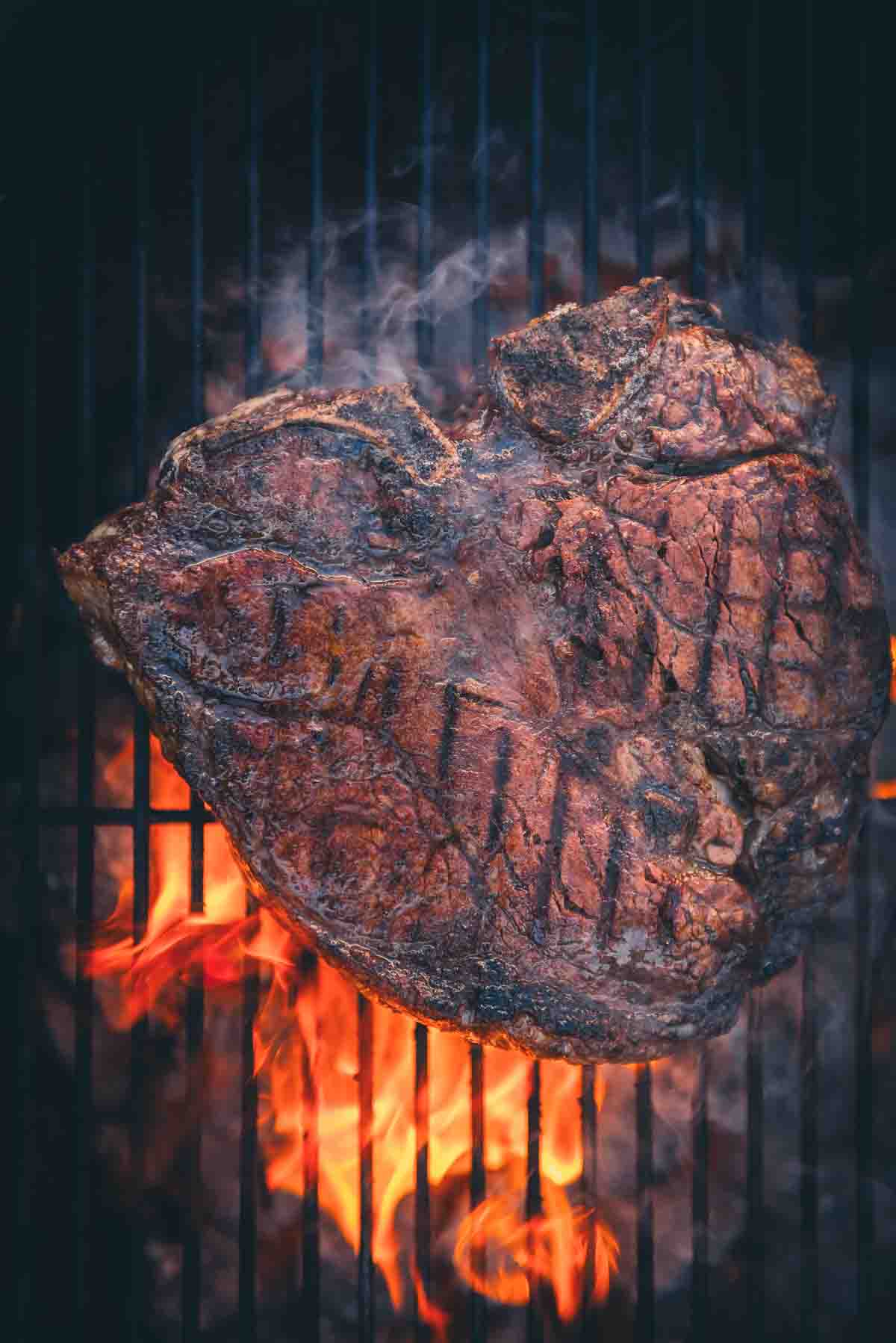 Overhead of porterhouse steak over flames showing grill marks.