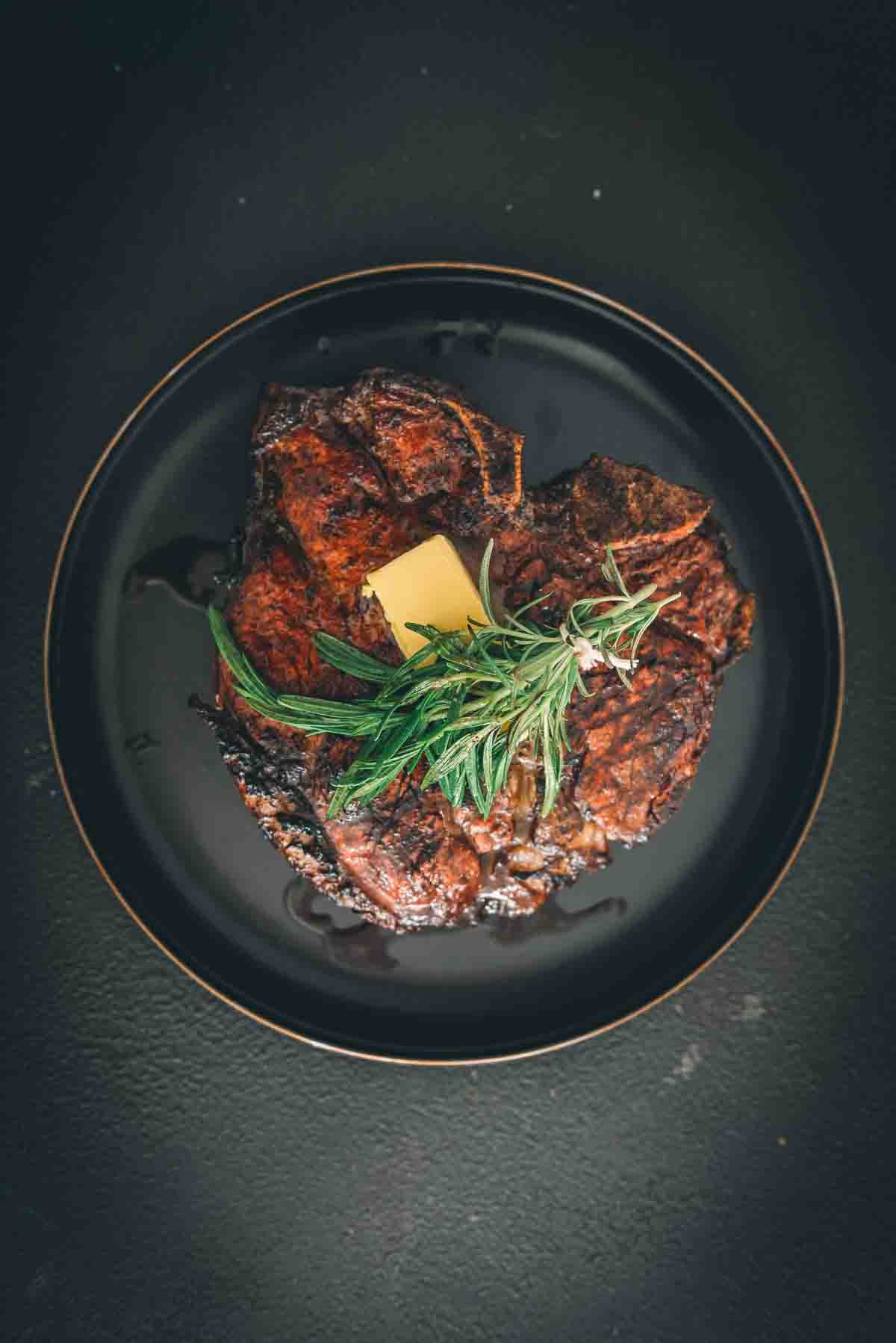 Grilled porterhouse resting on a plate with herbs and butter. 