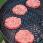 Hamburgers are being smoked on a grill.