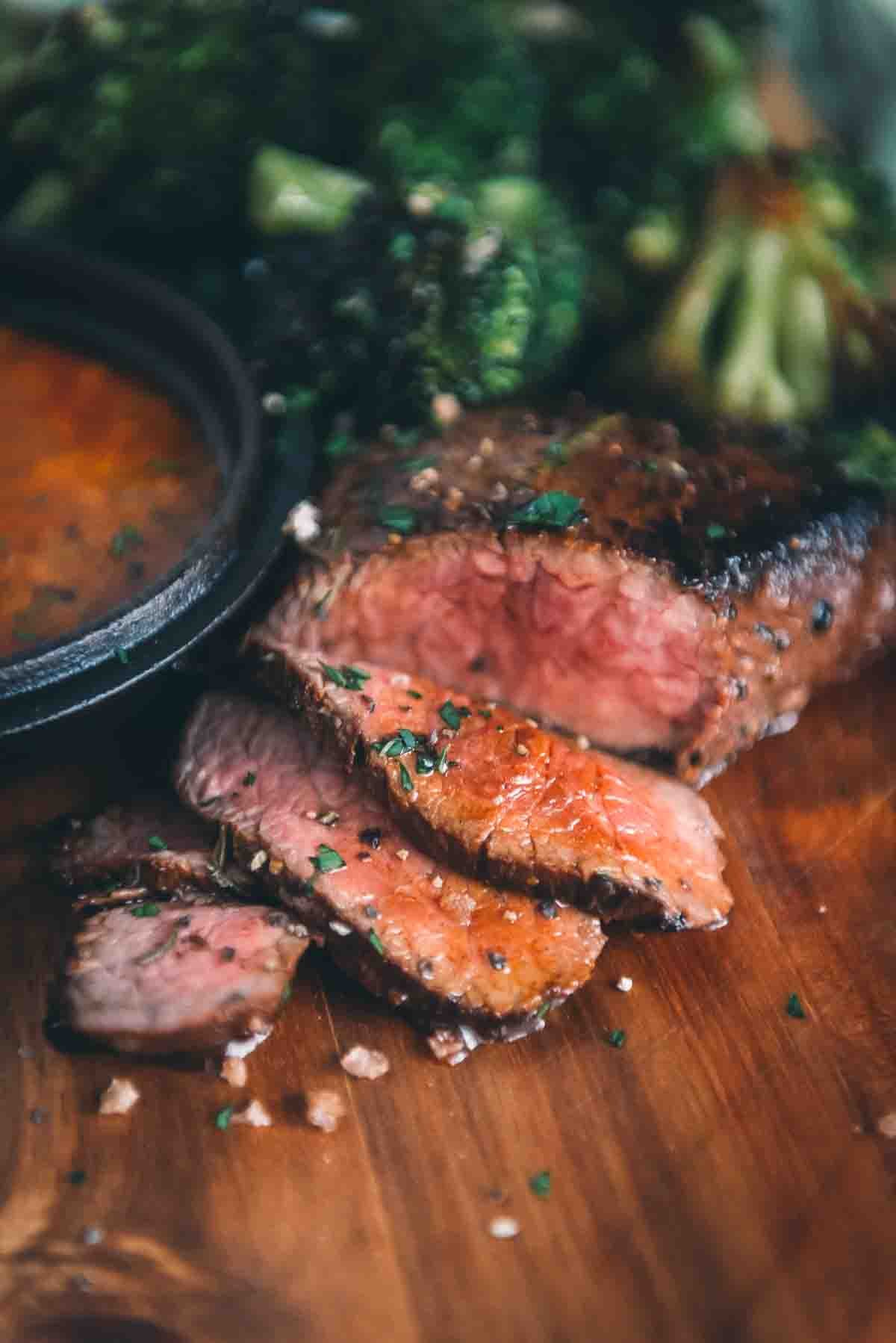 Close up of a pan seared ranch steak sliced into thin strips to show crust and pink center. 