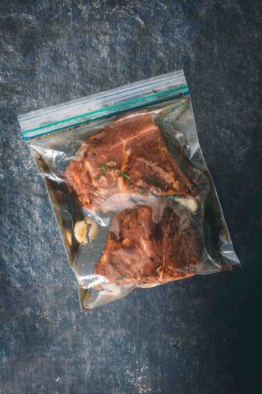Steak marinating in a plastic bag on a table.
