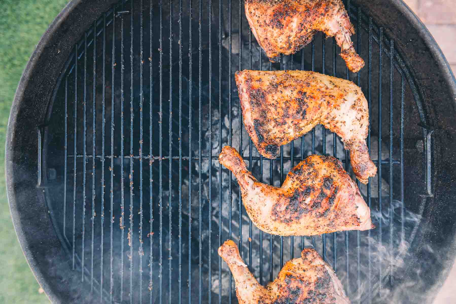 Chicken quarters on the grill after being moved to the hot side with wisps of smoke coming up.