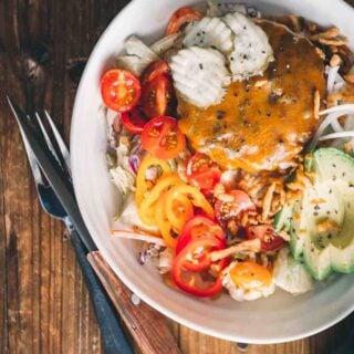 Overhead shot of big plate filled with crisp salad and a cheeseburger patty on top.
