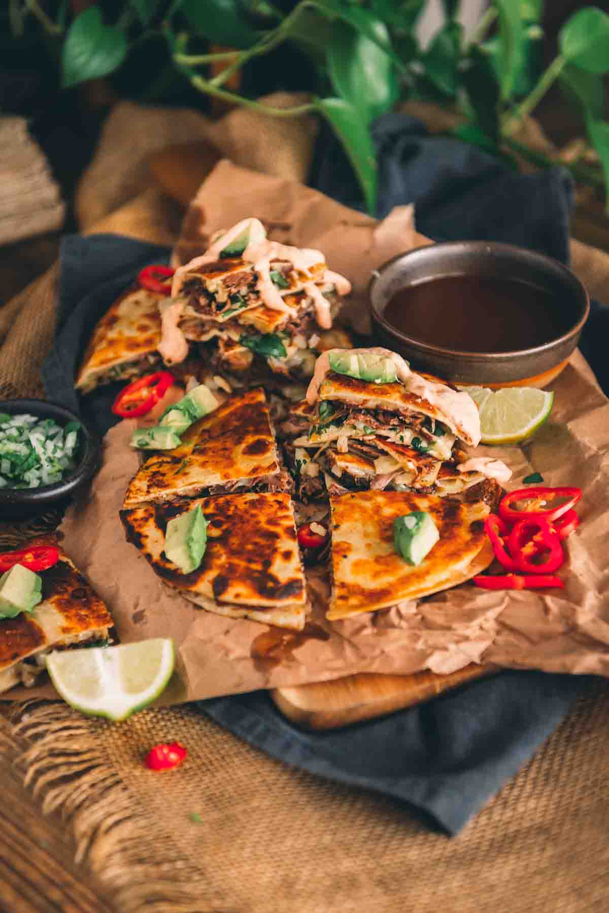 Platter of quesadillas sliced for serving with fresh toppings, crema and lime wedges. 